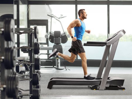 Foto de Largura completa de un hombre musculoso corriendo en una cinta de correr en el gimnasio - Imagen libre de derechos