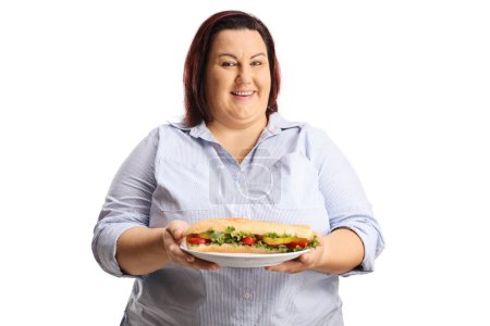 Téléchargez les photos : Femme en surpoids tenant un sandwich sur une assiette et souriant isolé sur fond blanc - en image libre de droit