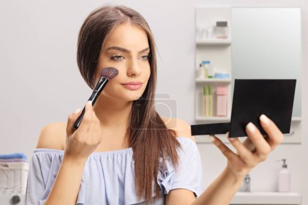 Téléchargez les photos : Jeune femme utilisant une brosse de maquillage dans une salle de bain - en image libre de droit