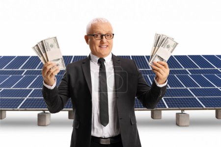 Foto de Hombre de negocios maduro sosteniendo pilas de billetes de dólar en una granja solar aislada sobre fondo blanco - Imagen libre de derechos