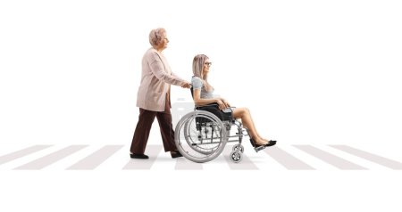 Téléchargez les photos : Plan de profil complet d'une femme âgée poussant une jeune femme en fauteuil roulant à un passage pour piétons isolé sur fond blanc - en image libre de droit