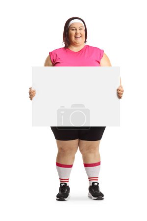 Téléchargez les photos : Femme en surpoids souriante en tenue de sport tenant une bannière vierge isolée sur fond blanc - en image libre de droit