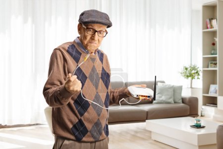 Téléchargez les photos : Homme plus âgé irrité tenant un câble routeur à la maison dans un salon - en image libre de droit