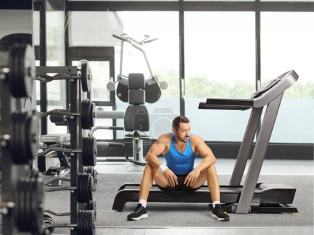Foto de Hombre atleta sentado en una cinta de correr y pensando en el gimnasio - Imagen libre de derechos