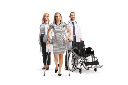 Photo for Woman with crutches standing in front of a medical team with a wheelchair isolated on white background - Royalty Free Image