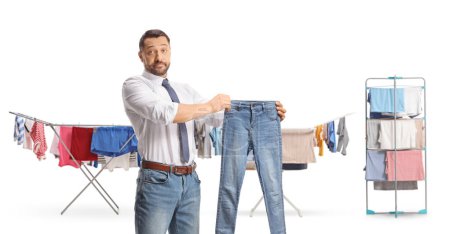Téléchargez les photos : Homme tenant une paire de jeans devant des rayonnages pour sécher des vêtements isolés sur fond blanc - en image libre de droit
