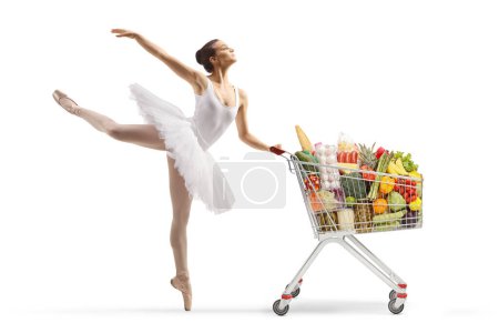 Photo for Full length profile shot of a ballerina in a white tutu dress dancing and pushing a shopping cart isolated on white background - Royalty Free Image