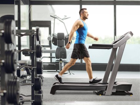 Photo for Full length profile shot of a young man walking on a treadmill inside a gym - Royalty Free Image