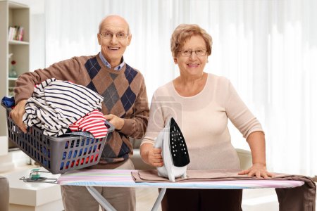Téléchargez les photos : Joyeux couple de personnes âgées repassage ensemble dans un salon - en image libre de droit