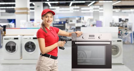 Photo for Repair woman with a drill standing next to an oven at a store - Royalty Free Image