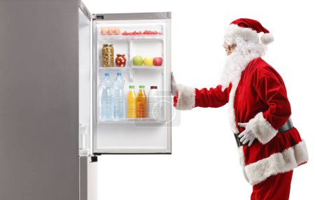 Foto de Santa Claus de pie frente a una nevera con alimentos aislados sobre fondo blanco - Imagen libre de derechos
