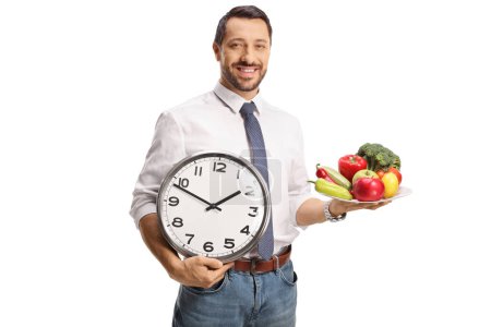 Foto de Hombre sosteniendo un plato con frutas y verduras y un reloj aislado sobre fondo blanco - Imagen libre de derechos