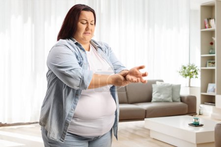 Photo for Worried overweight woman measuring pulse on hand wrist at home in a living room - Royalty Free Image