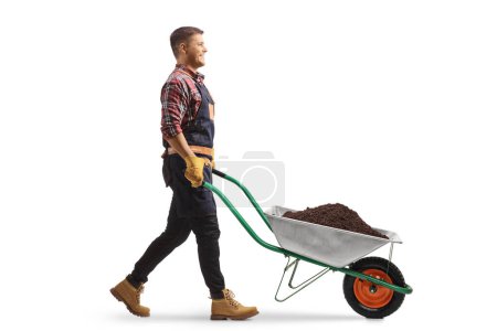 Foto de Foto de perfil completo de un granjero caminando con una carretilla llena de tierra aislada sobre fondo blanco - Imagen libre de derechos