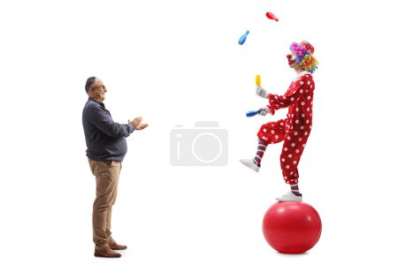 Téléchargez les photos : Plan de profil complet d'un homme mature applaudissant et regardant un clown jongler sur une balle isolée sur fond blanc - en image libre de droit