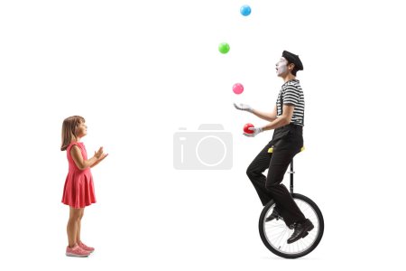 Téléchargez les photos : Petite fille applaudissant et regardant un mime jongler sur un monocycle isolé sur fond blanc - en image libre de droit