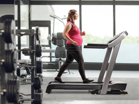 Photo for Full length profile shot of a pregnant woman running on a treadmill at a gym - Royalty Free Image