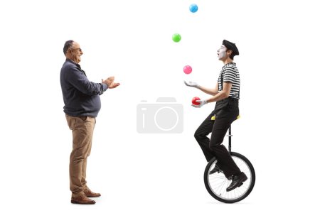 Photo for Full length profile shot of a mature man giving an applause to a mime on a unicycle juggling with balls isolated on white background - Royalty Free Image
