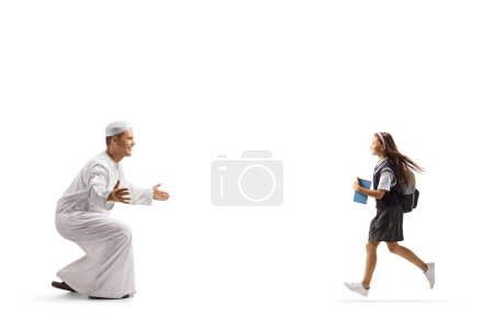 Téléchargez les photos : Écolière courant vers un homme en vêtements musulmans traditionnels isolé sur fond blanc - en image libre de droit