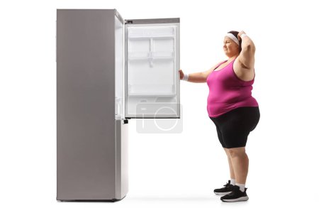 Photo for Pensive corpulent woman in sportswear looking inside an empty fridge isolated on white background - Royalty Free Image