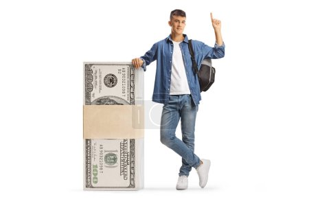Foto de Estudiante masculino apoyado en una pila de billetes de dólar y apuntando hacia arriba aislado sobre fondo blanco - Imagen libre de derechos