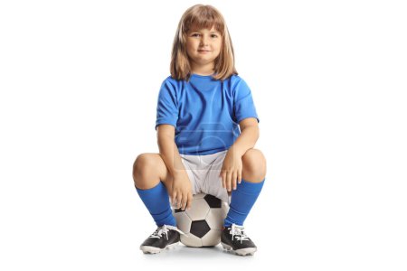 Photo for Full length profile shot of a cute little girl in a football kit sitting on a ball isolated on white background - Royalty Free Image