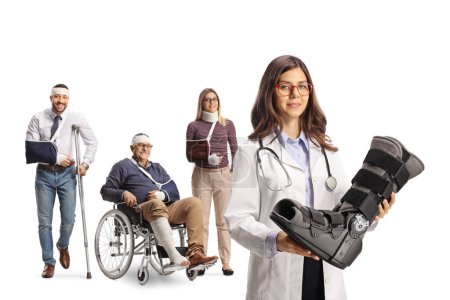 Téléchargez les photos : Jeune femme médecin tenant une orthèse du pied et groupe de personnes blessées debout derrière isolé sur fond blanc - en image libre de droit