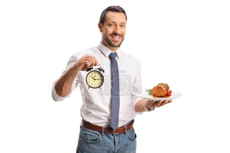Téléchargez les photos : Homme souriant et tenant de la viande cuite sur une assiette et une horloge isolée sur fond blanc - en image libre de droit