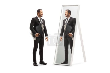Foto de Foto completa de un hombre de negocios de pie con un maletín lleno de dinero y mirando un espejo aislado sobre fondo blanco - Imagen libre de derechos