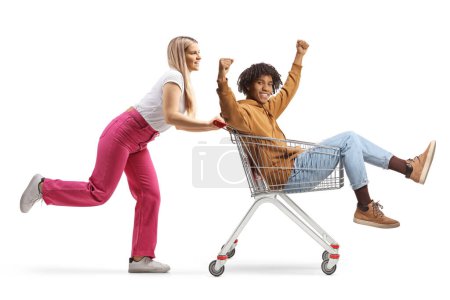 Photo for Caucasian young female pushing a shopping cart with an african american guy inside isolated on white background - Royalty Free Image