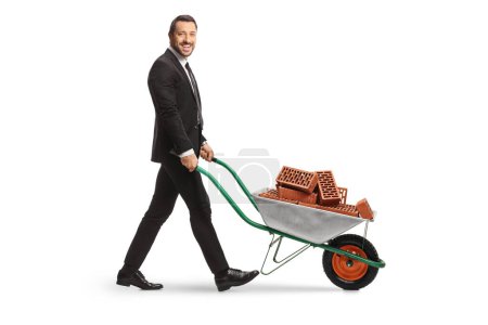 Photo for Businessman pushing a wheelbarrow with bricks isolated on white background - Royalty Free Image