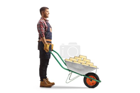 Photo for Full length profile shot of a farmer standing with gold in a wheelbarrow isolated on white background - Royalty Free Image