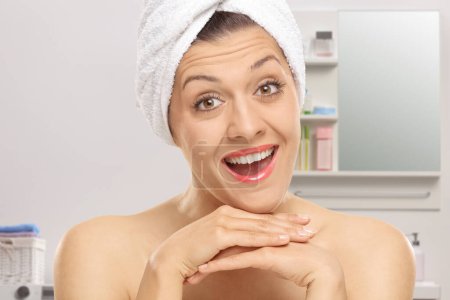 Téléchargez les photos : Gros plan d'une jeune femme avec une serviette sur la tête souriant dans une salle de bain - en image libre de droit