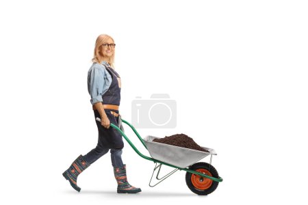 Photo for Female farmer walking with a wheelbarrow full of soil and looking at camera isolated on white background - Royalty Free Image