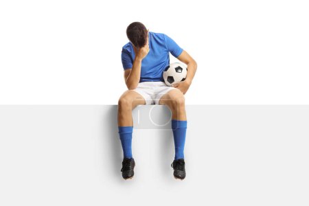 Foto de Triste jugador de fútbol sentado en un panel en blanco aislado sobre fondo blanco - Imagen libre de derechos