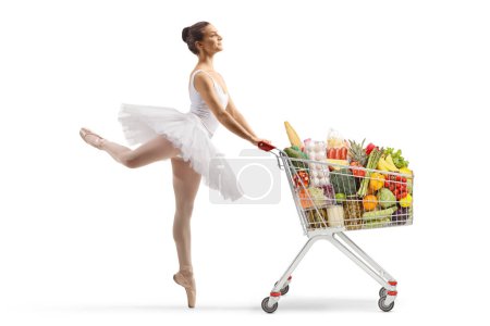 Téléchargez les photos : Photo de profil pleine longueur d'une ballerine dansant et poussant un chariot avec des produits alimentaires isolés sur fond blanc - en image libre de droit