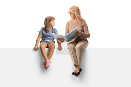 Photo for Woman reading a book to a little girl and sitting on a blank panel isolated on white backgroun - Royalty Free Image