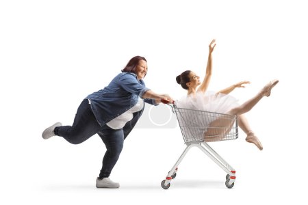 Foto de Mujer corpulenta empujando a una bailarina dentro de un carrito de compras aislado sobre fondo blanco - Imagen libre de derechos