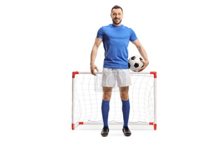 Foto de Retrato completo de un futbolista con una pelota bajo el brazo posando frente a un mini gol aislado sobre fondo blanco - Imagen libre de derechos