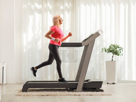 Photo for Full length profile shot of a mature woman running on a treadmill at home - Royalty Free Image