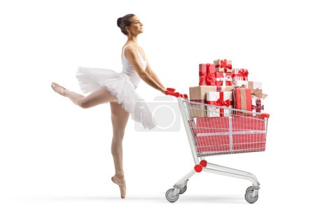 Foto de Foto de perfil completo de una bailarina bailando y empujando un carrito de compras con regalos aislados sobre fondo blanco - Imagen libre de derechos