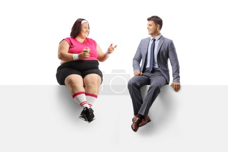 Téléchargez les photos : Femme de taille plus en tenue de sport tenant un shake vert sain et parlant à un homme d'affaires isolé sur fond blanc - en image libre de droit