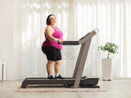 Photo for Smiling young corpulent woman standing on a treadmill in a room and looking at camera - Royalty Free Image