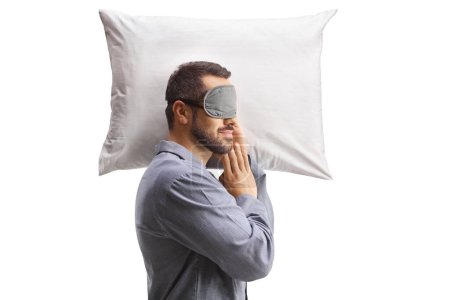 Téléchargez les photos : Homme en pyjama dormant avec un masque sur un oreiller isolé sur fond blanc - en image libre de droit