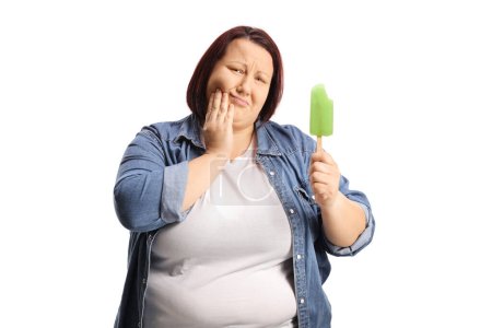 Téléchargez les photos : Femme corpulente avec une crème glacée sucette tenant sa joue et ayant un mal de dents isolé sur fond blanc - en image libre de droit