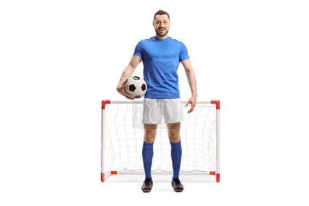 Foto de Retrato completo de un jugador de fútbol sosteniendo una pelota frente a un mini gol aislado sobre fondo blanco - Imagen libre de derechos