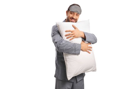 Téléchargez les photos : Homme heureux en pyjama avec un masque de sommeil étreignant un oreiller et souriant isolé sur fond blanc - en image libre de droit
