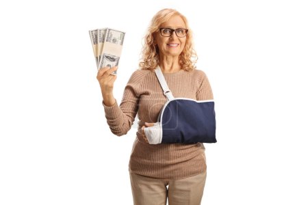 Photo for Woman with a broken arm in a sling holding stacks of money isolated on white background - Royalty Free Image