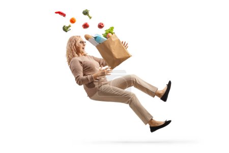 tiro de longitud completa de una mujer con una bolsa de comestibles cayendo aislado sobre fondo blanco