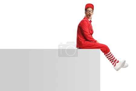 Photo for Funny entertainer in a red suit sitting on a wall isolated on white background - Royalty Free Image